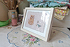medium sized framed textile picture of a cat and a bird holding a flower